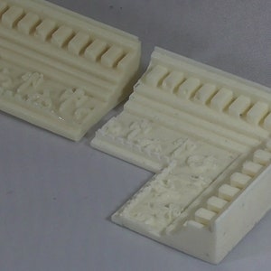 May include: Two pieces of white, decorative moulding with an ornate design. The moulding has a raised pattern of leaves and flowers.