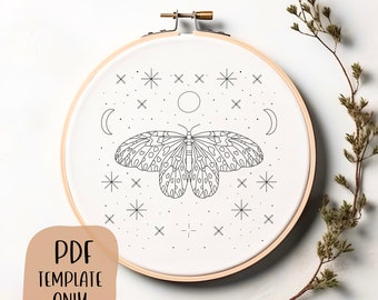 Può includere: Un disegno in bianco e nero di una farfalla con una luna e stelle su sfondo bianco. Il disegno è in un telaio da ricamo in legno.