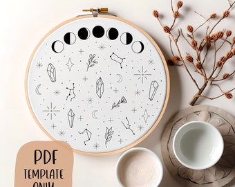 Può includere: Un motivo di ricamo in bianco e nero con un design di fasi lunari, cristalli, stelle e costellazioni. Il motivo è stampato su un tessuto bianco ed è esposto in un telaio da ricamo in legno. Il testo "PDF TEMPLATE ONLY" è stampato su uno sfondo marrone.