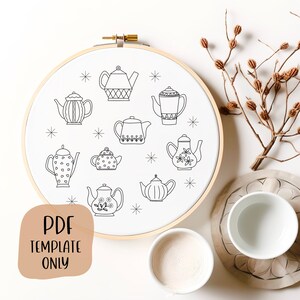 May include: A white embroidery hoop with a black and white line drawing of nine different teapots. The teapots are all different shapes and sizes, and some have decorative details. The hoop is on a white surface with a brown branch and two white cups.