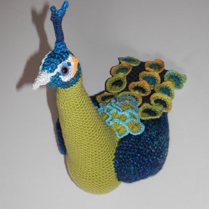 May include: A crocheted peacock stuffed toy with a green body, blue tail feathers, and a white face with a blue crest.