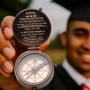Puede incluir: Una brújula de estilo vintage con acabado en bronce oscuro. La esfera de la brújula muestra marcas direccionales. La tapa tiene grabado el nombre "Ethan" y el mensaje "Wherever your journey...Love, Mom & Dad."