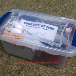May include: A clear plastic storage container with a blue lid. The container is filled with various items, including a certificate that reads "Shoe Box of Fire Certificate of Shoe Goodness".