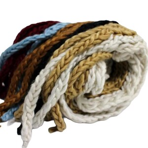 May include: A rolled bundle of thick, braided yarn in various colors. The colors include burgundy, light blue, brown, black, tan, and white. The yarn appears to be made of a soft, chunky material, suitable for crafting projects.