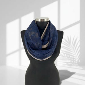 May include: A navy blue lace infinity scarf with a tan lining is displayed on a black mannequin. The scarf is draped in a circular fashion, showcasing the intricate floral lace pattern. The scarf is a fashion accessory.