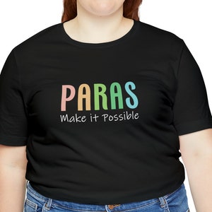May include: A black short-sleeved t-shirt featuring the word PARAS in a multi-colored gradient font above the white text Make it Possible. The shirt is paired with blue denim jeans, creating a casual look with clear, legible lettering.
