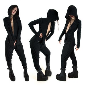 Puede incluir: Tres mujeres con monos negros con capucha y cremallera en la parte delantera. Los monos tienen mangas largas y un corte holgado. Las mujeres llevan botas de plataforma negras.