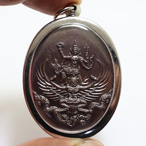 Könnte beinhalten: Ein silberner ovaler Anhänger mit einem braunen Metalldesign einer mythischen Kreatur mit Flügeln und einer menschlichen Figur oben. Der Anhänger hat eine Schlaufe oben zum Anbringen einer Kette.