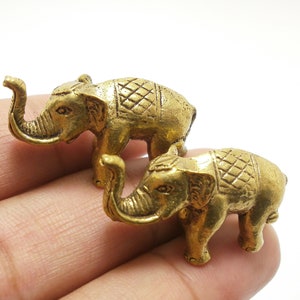 May include: Two small gold-colored elephant figurines with intricate details. The elephants have raised trunks and are standing on a hand.