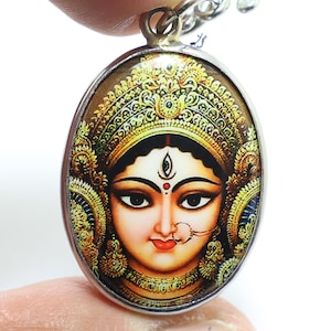 May include: A silver oval pendant with a colorful image of a Hindu goddess with a golden crown and ornate jewelry. The pendant is on a silver chain.