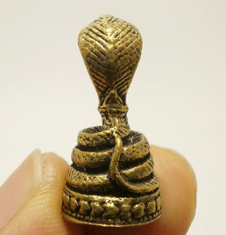 Puede incluir: Una figurita de metal de color dorado que representa una cobra con la cabeza levantada y el cuerpo enroscado en espiral. La figurita est&aacute; detallada con escamas y tiene una base decorativa.