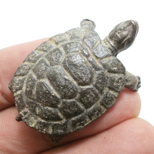 May include: A small, gray, metal turtle figurine with a detailed shell and a raised head. The turtle is about 2 inches long.