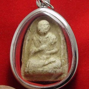 May include: A silver pendant with a white ceramic Buddha figurine inside. The Buddha is sitting in a meditative pose with hands clasped in front of the chest.