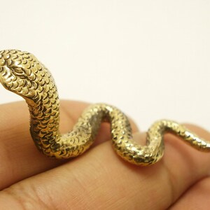 May include: A gold-colored metal snake figurine with a coiled body and a raised head. The snake is detailed with scales and has a realistic appearance.
