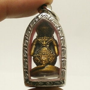 Pu&ograve; includere: Un ciondolo di amuleto Buddha color oro racchiuso in una cornice di plastica trasparente e argento. Il ciondolo ha la forma di un Buddha in piedi con dettagli intricati.