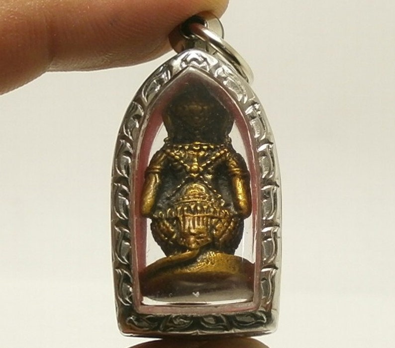 Pu&ograve; includere: Un ciondolo di amuleto Buddha color oro racchiuso in una cornice di plastica trasparente e argento. Il ciondolo ha la forma di un Buddha in piedi con dettagli intricati.