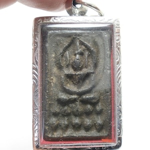 Może przedstawiać: Srebrny wisiorek z ciemnoszarym prostokątnym amuletem w środku. Amulet ma wypukły wzór przedstawiający postać z koroną i wzorem kwiatowym.