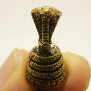 May include: A small, gold-colored metal figurine of a cobra with its hood raised. The cobra is standing on a base with a coiled snake design.