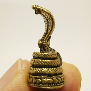 Puede incluir: Una peque&ntilde;a figura de metal dorada de una cobra con la cabeza levantada y la capucha expandida. La serpiente est&aacute; enroscada alrededor de una base con intrincados detalles.