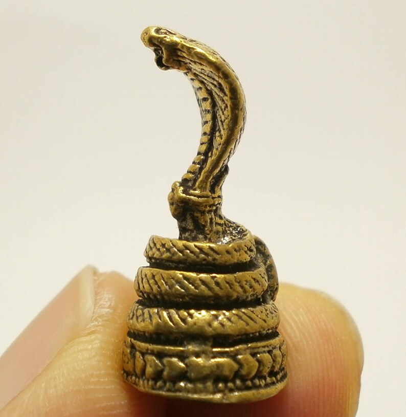 Puede incluir: Una peque&ntilde;a figura de metal dorada de una cobra con la cabeza levantada y la capucha expandida. La serpiente est&aacute; enroscada alrededor de una base con intrincados detalles.