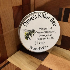 May include: A white round tin with a black and white label that says "Dave's Killer Bee Wood Wax (1 oz)". The label also lists the ingredients: mineral oil, organic beeswax, orange oil, and peppermint oil. A cartoon bee is pictured on the label.