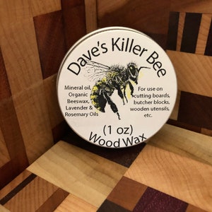 May include: A white tin with a yellow and black bee illustration and the text "Dave's Killer Bee Wood Wax (1 oz)". The tin contains a wood wax for use on cutting boards, butcher blocks, wooden utensils, and more.