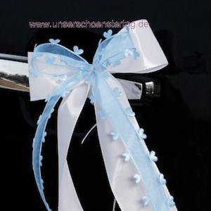 May include: A white satin ribbon with a blue sheer ribbon with small flower accents. The ribbon is tied in a bow and has the text "www.unser schoenster tag.de" printed on it. The ribbon is tied to a car door handle.