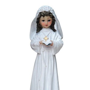 May include: White figurine of a girl in a white dress and veil holding a book with a cross on it.
