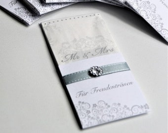 Può includere: Un pacchetto di fazzoletti di carta bianca con un design floreale argento e grigio. I pacchetti sono legati con un nastro blu chiaro e hanno il testo "Mr & Mrs" e "Für Freudentränen" stampato su di essi.