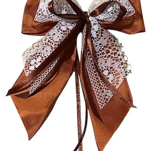 May include: A brown satin bow with white lace accents. The bow has a long tail for attaching to a gift or other item.