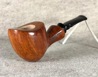 May include: A brown wooden pipe with a black mouthpiece. The pipe is marked "Dunhill's" and "De Luxe".
