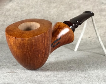 May include: A wooden tobacco pipe with a rounded bowl and a dark brown stem. The bowl is a light brown color with visible wood grain. The stem is curved and has a smooth, glossy finish. The pipe is resting on a gray surface.