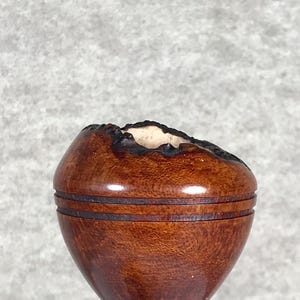 May include: A handcrafted wooden bowl with a dark brown finish. The bowl has a rounded shape with a textured rim and a black base. The wood grain is visible, adding to its natural aesthetic. The bowl is likely used for decorative purposes.
