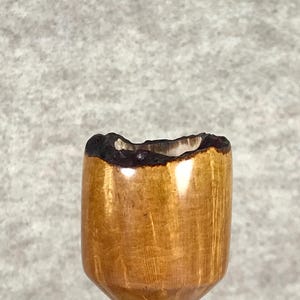 Puede incluir: Un cuenco de pipa de madera artesanal con un borde marrón oscuro texturizado. El cuenco tiene un acabado marrón claro pulido y se asienta sobre una base negra. La pipa está diseñada para fumar y es un accesorio de tabaco tradicional.