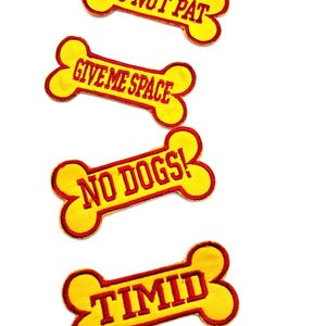 May include: Four yellow bone-shaped patches with red text. The patches read: "DO NOT PAT", "GIVE ME SPACE", "NO DOGS!", and "TIMID". The patches have a red border and are set against a white background.