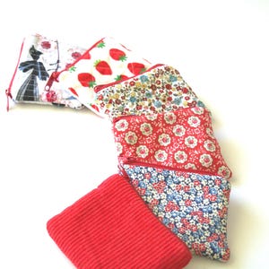 May include: A selection of small, zipped pouches in diverse floral and patterned fabrics. Designs include strawberries, a silhouette, and red floral prints. One pouch is a solid red corduroy.