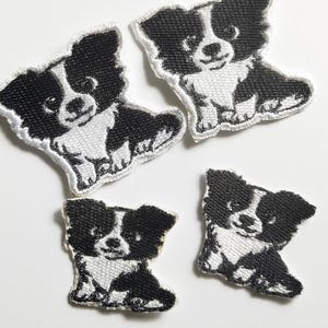 May include: Four embroidered patches featuring a black and white puppy design. The patches are in the shape of a sitting dog with a smiling face. The patches are white with black accents.