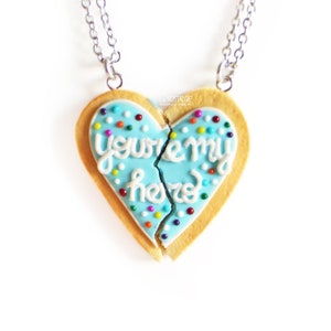 May include: A pair of best friend necklaces with a blue and white heart-shaped cookie charm that says "you're my other half". The cookie is broken in half and each half is on a separate chain.