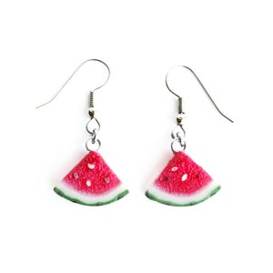 May include: A pair of silver dangle earrings with watermelon slice charms. The watermelon slices are red with black seeds and a green rind.