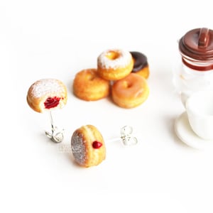 May include: Donut-themed jewelry set featuring two donut earrings, a small coffee pot, and a cup and saucer. The donuts have various toppings, including powdered sugar and glaze. One earring has a bite taken out, revealing a red filling.