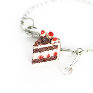 Peut inclure: Un bracelet en chaîne argent avec un charme en forme de part de gâteau au chocolat avec des cerises rouges et un glaçage blanc. Le charme est attaché à une petite cuillère en argent.