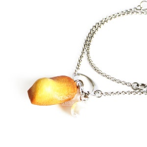 Puede incluir: Un brazalete de cadena plateada con un dije de madeleine amarilla y naranja y una perla blanca.