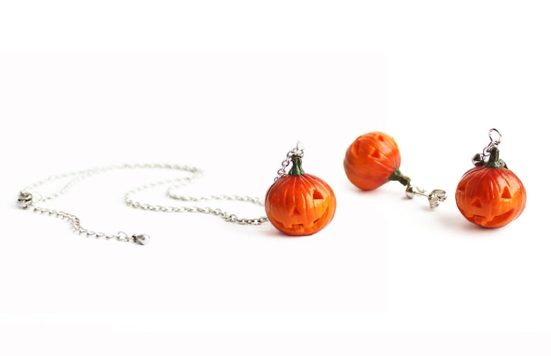 May include: A set of Halloween jewelry featuring orange pumpkin earrings and a necklace with a pumpkin pendant. The pumpkins have carved faces and are made of polymer clay.