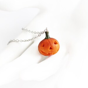 May include: A silver chain necklace with a small orange pumpkin pendant. The pumpkin has a carved jack-o'-lantern face.