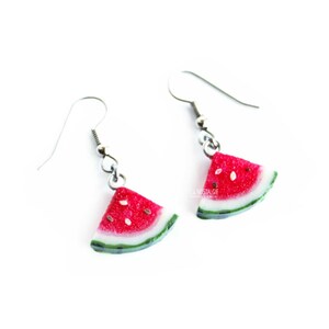 May include: A pair of silver dangle earrings with watermelon slice charms. The watermelon slices are red with black seeds and a green rind.