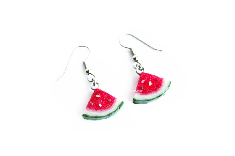 May include: A pair of silver dangle earrings with watermelon slice charms. The watermelon slices are red with black seeds and a green rind.