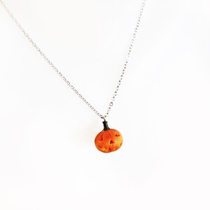 May include: A silver chain necklace with a small orange pumpkin pendant. The pumpkin has a carved face with a black stem.