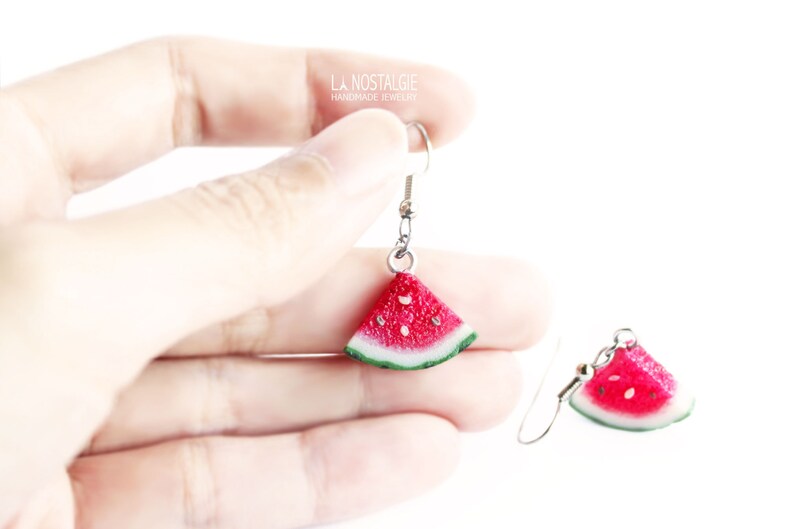 May include: A pair of silver dangle earrings with watermelon slice charms. The watermelon slices are red with black seeds and green rind.