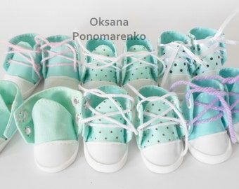 May include: A set of eight miniature baby shoes in various colors, including mint green, white, pink, and purple. The shoes have white laces and some have white polka dots.
