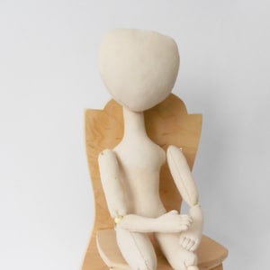 May include: A white fabric doll with jointed limbs sits on a wooden chair. The doll has a simple, unpainted face and is ready for customization.